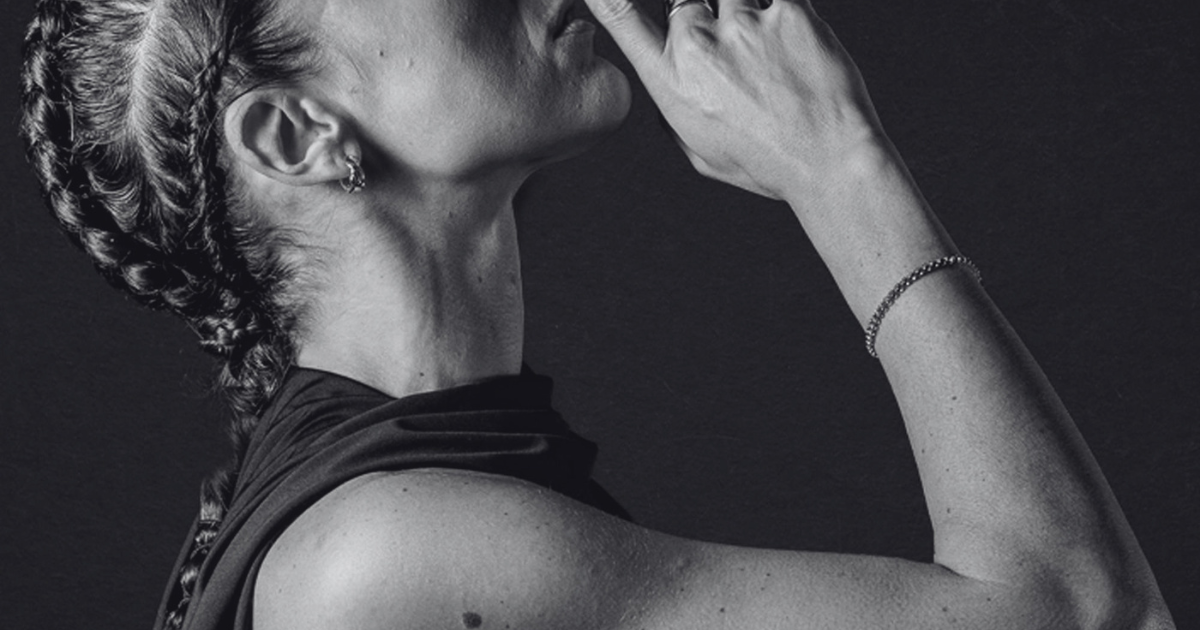 Black-and-white editorial profile of a woman with braids raising her hand to her face against a dark backdrop